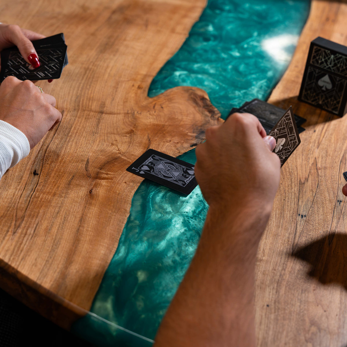 Hands playing a game of cards with the LGND Playing Cards at a wood and resin table